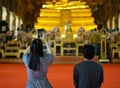 Young Asian couples tourists worship and taking photo of golden Buddha statue.