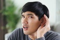 Young Asian deaf disabled man having hearing problems holds his hand over the ear, listens carefully, hard of hearing
