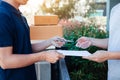 Young asian delivery staff holding the pen and documents submitting giving to the customer receiving the parcel at front house