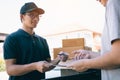 Young asian delivery staff holding the pen and documents submitting giving to the customer receiving the parcel at front house