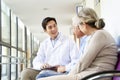 Young asian doctor talking to senior couple patients in hospital hallway