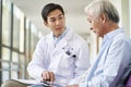 Young asian doctor talking to senior man in hospital hallway Royalty Free Stock Photo