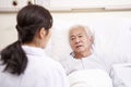 Young asian doctor talking to senior patient at bedside in hosptal ward Royalty Free Stock Photo