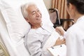 Young asian doctor talking to senior patient at bedside in hosptial ward Royalty Free Stock Photo