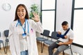 Young asian doctor woman at waiting room with a man with a broken arm showing and pointing up with fingers number five while Royalty Free Stock Photo
