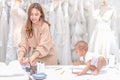 Young Asian dressmaker mother sews clothes with little baby sitting near her. Single mother take care daughter while working at