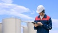Young Asian engineer using digital tablet with blurred storage fuel tanks against cloud on blue sky background Royalty Free Stock Photo