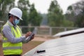 A young Asian engineer wearing a helmet and white mask checks the cleanliness of solar panels Royalty Free Stock Photo