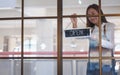 A young entrepreneur or a waitress hanging open sign on the shop front door