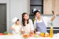 Young Asian family are preparing salad in the kitchen and father take a photo selfie by phone. Excited smiling and felling happy.