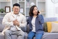 Young Asian family sitting on sofa at home. A man holds his hand to his chest, heart attack, stroke, panic attack, feels Royalty Free Stock Photo