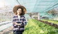 Young Asian farmer pretty girl working in vegetables hydroponic farm with happiness. She is looking and using hands Royalty Free Stock Photo