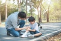 Young asian father of dad calms son that fell from the bike and he get injury on knee and leg while have weekend leisure in public