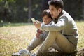 Young asian father and son looking at cellphone together oudoors in park Royalty Free Stock Photo