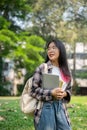 A young Asian female college student carrying a backpack and stuff, standing in the campus park Royalty Free Stock Photo