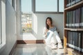 Young asian female college student sitting on floor in library, reading book Royalty Free Stock Photo