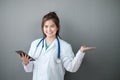 A young Asian female doctor holding a tablet standing on a grey background. Royalty Free Stock Photo