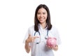 Young Asian female doctor point to a pig bank coin. Royalty Free Stock Photo