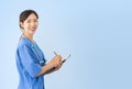 Asian female doctor wearing lab coat and stethoscope smiles as she is writing on medical folder Royalty Free Stock Photo