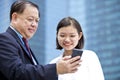 Young Asian female executive and senior businessman using smart phone