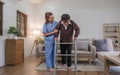 young asian female nurse care giver helping asian senior old man with mobility walker in living area of nursing home Royalty Free Stock Photo