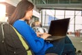 Young Asian female passenger using laptop and smart phone while sitting on seat in terminal hall and waiting for flight in airport Royalty Free Stock Photo