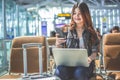 Young Asian female passenger using laptop and smart phone while sitting on seat in terminal hall and waiting for flight in airport Royalty Free Stock Photo