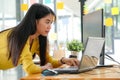 Young Asian female programmer in a yellow shirt stands down to use her laptop and PC in the office
