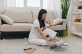 Young Asian female student looking at laptop screen sitting on floor at home with notebooks to write, lifestyle work