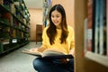 Young Asian female student reading book in library for studying, knowledge and literature research Royalty Free Stock Photo