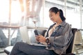 Young Asian female tourist look at smart phone with her laptop at airport