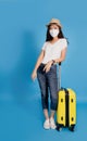 Young Asian female traveler wearing masks and summer casual attire with yellow suitcase isolated on blue background. She was Royalty Free Stock Photo