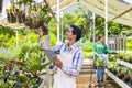 Young Asian garden owner is checking hanging orchid plant from the his garden center nursery with custormer`s shopping cart for