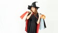 Young asian girl with black and orange hair in black dress and witch hat is holding shopping bags and smiling on white background Royalty Free Stock Photo