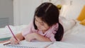 Young Asian girl drawing at home. Asia japanese woman child kid relax rest fun happy draw cartoon in sketchbook before sleep lying