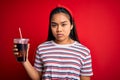 Young asian girl drinking cola fizzy refreshment using straw over isolated red background with a confident expression on smart Royalty Free Stock Photo