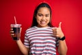 Young asian girl drinking cola fizzy refreshment using straw over isolated red background happy with big smile doing ok sign, Royalty Free Stock Photo