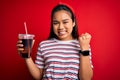 Young asian girl drinking cola fizzy refreshment using straw over isolated red background screaming proud and celebrating victory Royalty Free Stock Photo