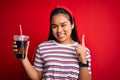 Young asian girl drinking cola fizzy refreshment using straw over isolated red background surprised with an idea or question Royalty Free Stock Photo