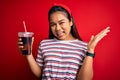 Young asian girl drinking cola fizzy refreshment using straw over isolated red background very happy and excited, winner Royalty Free Stock Photo