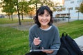 Young asian girl with graphic pencil and tablet, sits in park on bench, draws scatches, does her homework outdoors Royalty Free Stock Photo