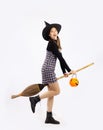 Young asian girl in halloween costume wearing black witch hat holding pumpkin lantern and witch broom posing on white background Royalty Free Stock Photo