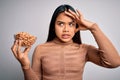 Young asian girl holding bowl of healthy peanuts eating as snack for diet over white background stressed with hand on head, Royalty Free Stock Photo