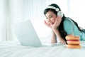 Young Asian girl lying in bed watching a program on laptop monitor with donuts served aside