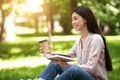 Young asian girl reading book and drinking takeaway coffee in park outdoors Royalty Free Stock Photo