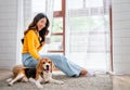 Young Asian girl sit on seat cushion also hold cup of tea and enjoy to play with beagle dog in front of glass door of the house Royalty Free Stock Photo