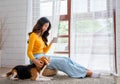 Young Asian girl sit on seat cushion also hold cup of tea and enjoy to play with beagle dog in front of glass door of the house Royalty Free Stock Photo
