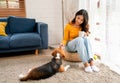 Young Asian girl sit on seat cushion also hold cup of tea and enjoy to play with beagle dog in front of glass door of the house Royalty Free Stock Photo