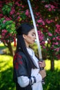 Young asian girl in traditional kimano in a blooming garden with samurai japanese sword katana in image of warrior woman Royalty Free Stock Photo