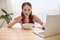 Young Asian girl using laptop while having noodles at home Royalty Free Stock Photo